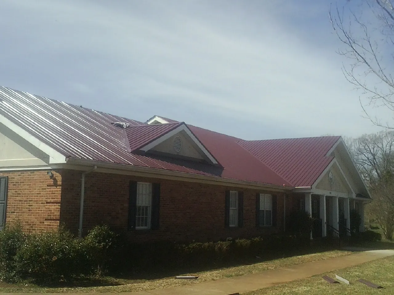 Red metal roof with gabled entries on a long brick building, from a Hail Damage Roof Repair job in Antwerp