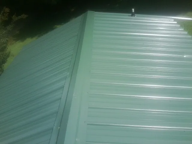 New green metal panels meeting at the ridge of a roof — Flat Roof Repair work by our crew in Antwerp